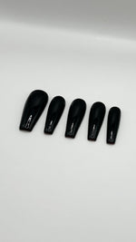 A top-down product photograph of five custom press-on nails in a long coffin shape, arranged on a clean white background. The nails feature a flawless, high-gloss jet black gel finish with a perfectly sculpted, smooth salon architecture.