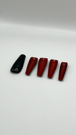 A close-up product photograph highlighting the underside of long custom press-on nails. While the top layer is a high-gloss jet black, the hidden bottom layer is painted a vibrant, solid crimson red, creating a luxury two-tone designer effect.