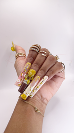 Extra-long, square press-on nails with a honeybee and honey pot theme. The pinky nail features a milk-white base decorated with a trail of tiny painted bees. The ring finger has a nude base with a glossy yellow honey-drip French tip and painted bees. The middle finger is painted dark brown to look like a honey pot with the word "HUNNY" and a massive, raised 3D hand-sculpted yellow honey drip. The index finger has a soft pink base with yellow honey drips, 3D white flowers, and painted bees.