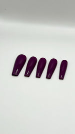 A top-down product photograph showing a set of five long, high-gloss purple press-on nails arranged neatly in a row. The salon-grade gel nails are displayed on a clean, solid white background, showcasing their crisp shape, rich solid plum purple color, and a flawless, reflective glass-like top coat.