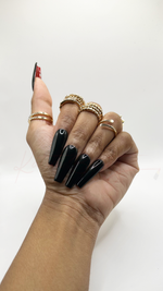 Medium coffin-shaped press-on nails with a smooth, solid glossy black polish finish on all fingers. The underside of the thumb nail features a hidden bright red accent color.